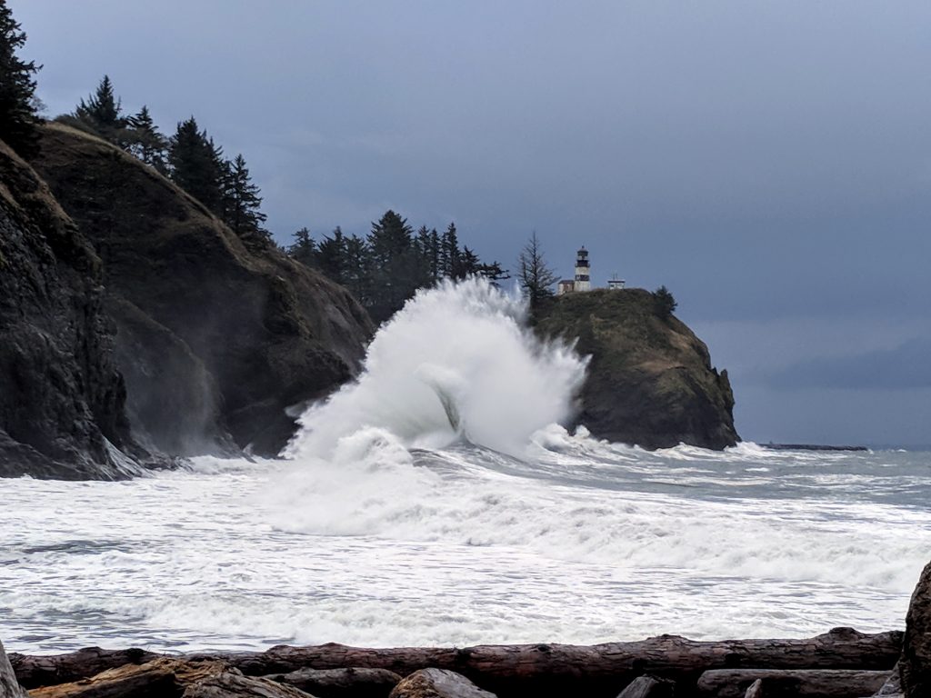 A big wave crashes beneath the Cape Disappointment Lighthouse