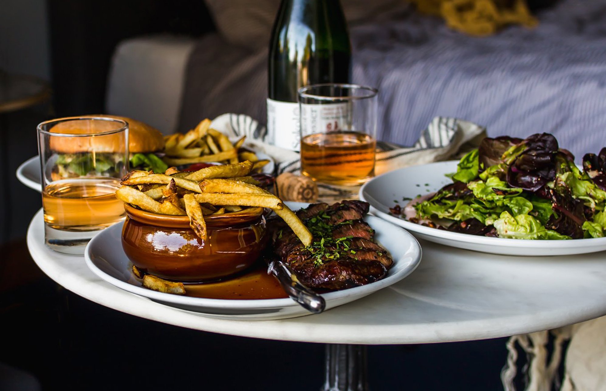 A platter carrying plates with fries and steak, a burger, a salad and a bottle and glass.