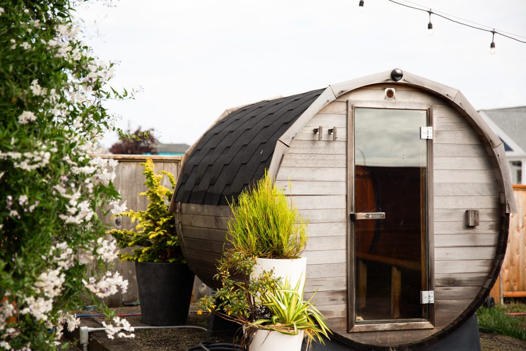 A small, wooden outdoor sauna surrounded by plants.